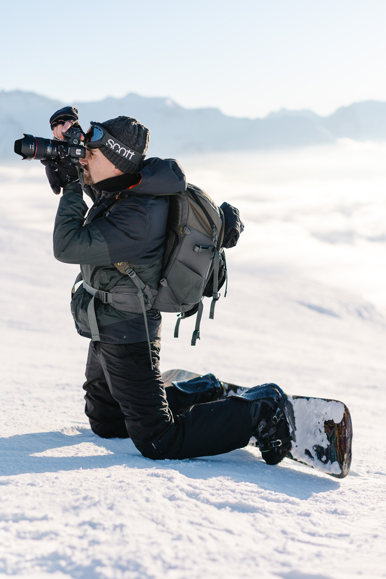 Un snowboarder à genoux dans la neige en train de prendre une photo