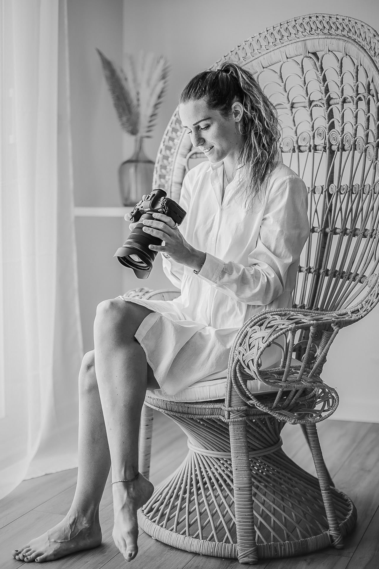 Une femme est assise sur un fauteuil en rotin avec un appareil photo dans les mains